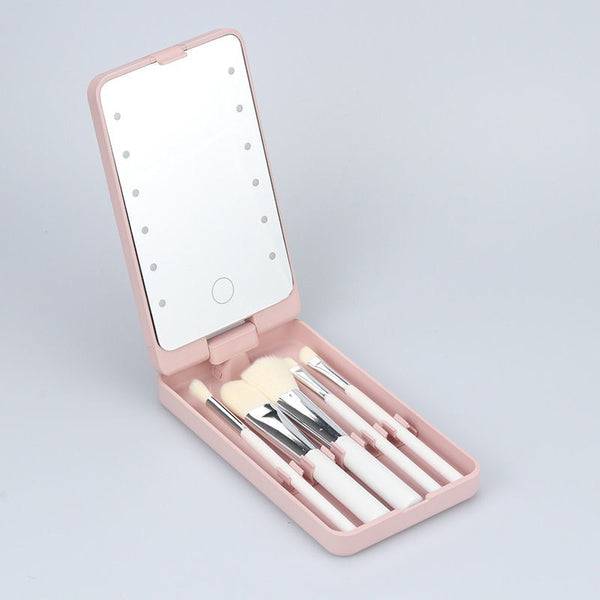 A pink portable makeup kit with a built-in mirror and several makeup brushes neatly arranged inside. The kit is open, showing the brushes and the illuminated mirror